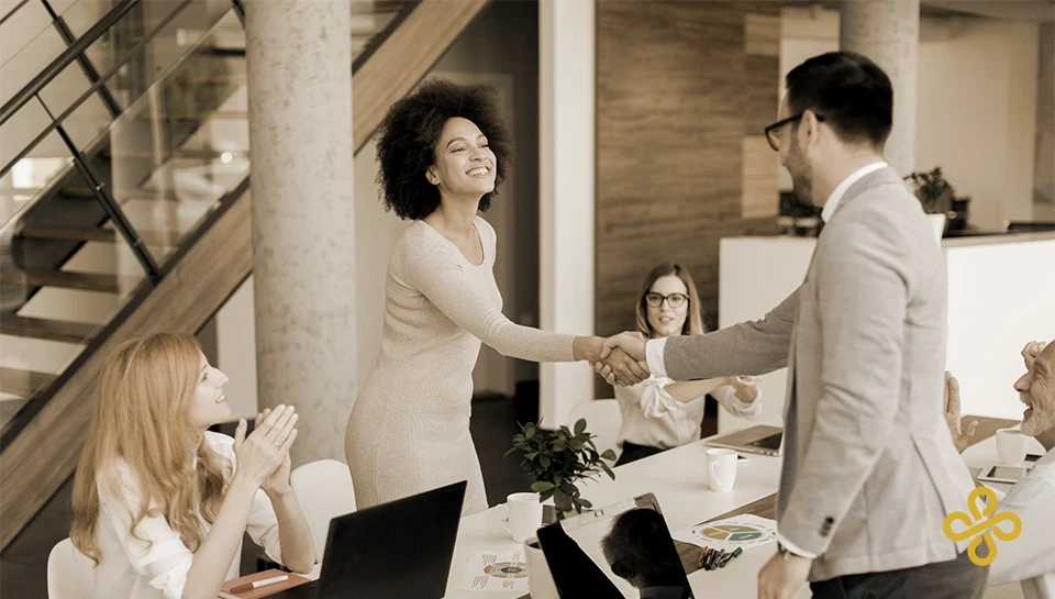 A lady and a man shaking hands over a meeting table, signifying a done deal