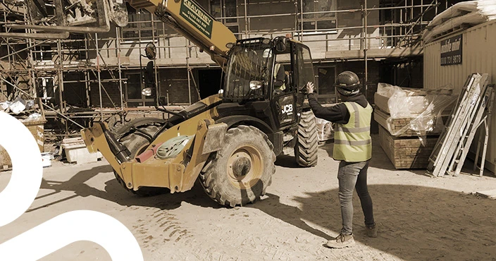 A vehicle banksman directing a yellow excavator