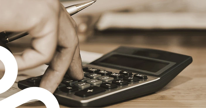A hand holding a pen and using a calculator