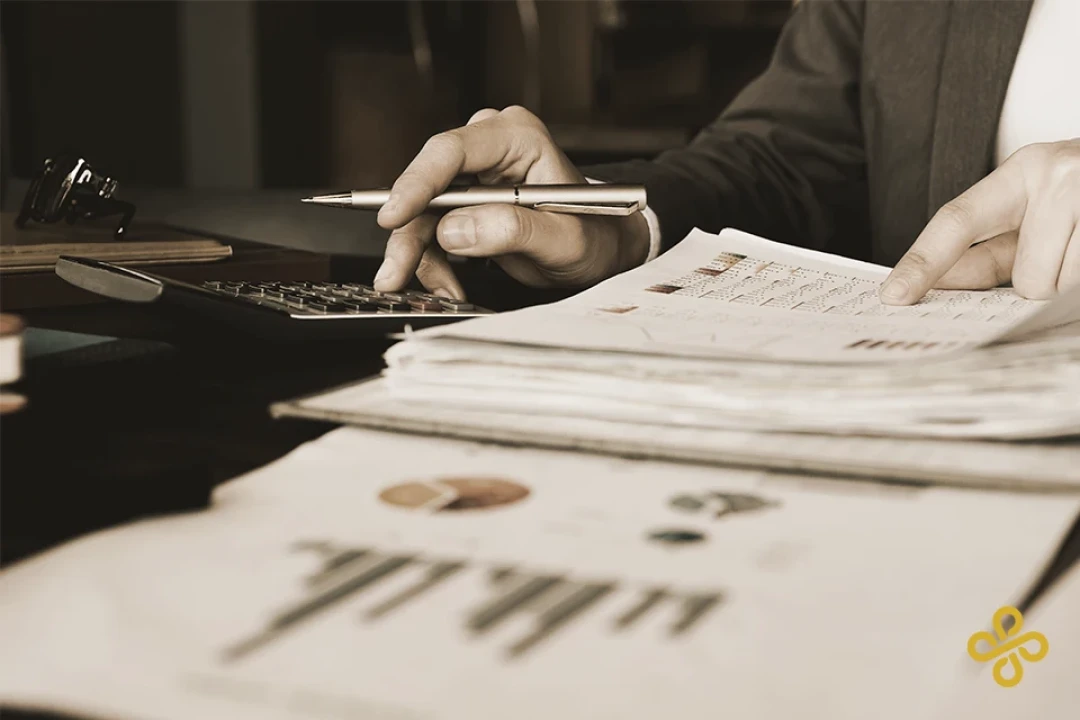 Close-up shot of a man looking at paperwork and using a calculator.